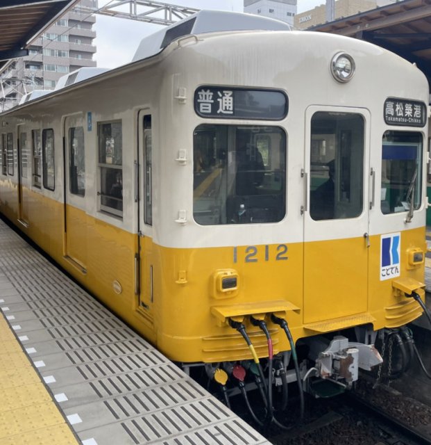 駅ホームに停車する黄色とクリーム色のことでん車両1212号