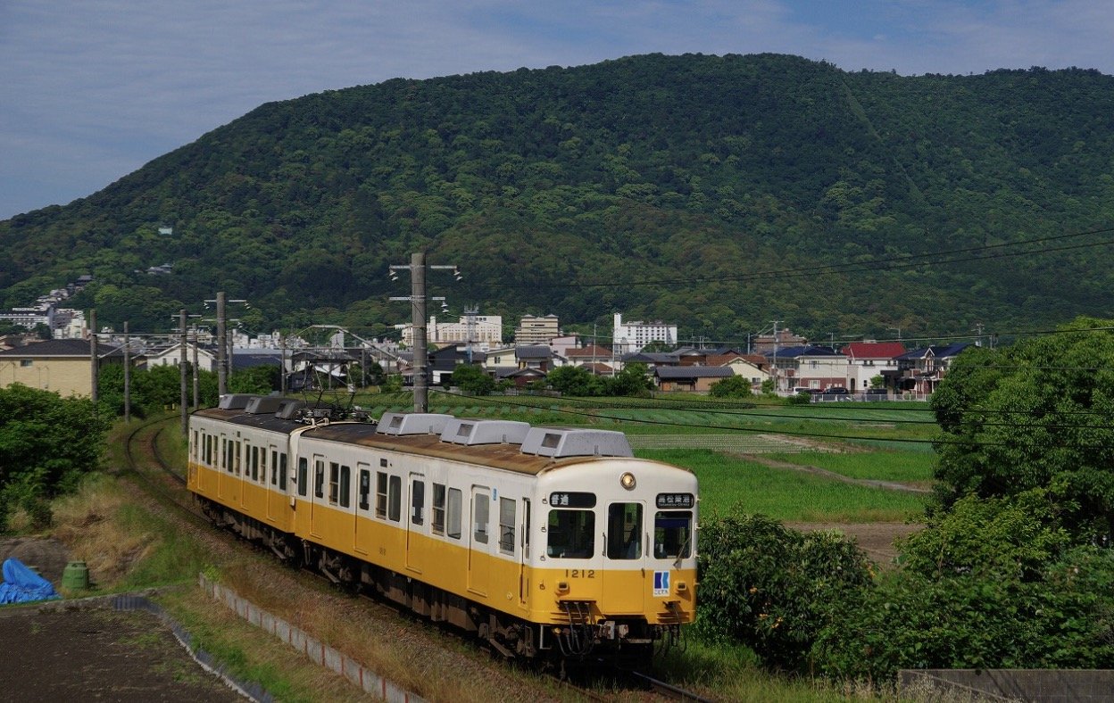 山を背景に走る黄色とクリーム色のことでん車両1212号